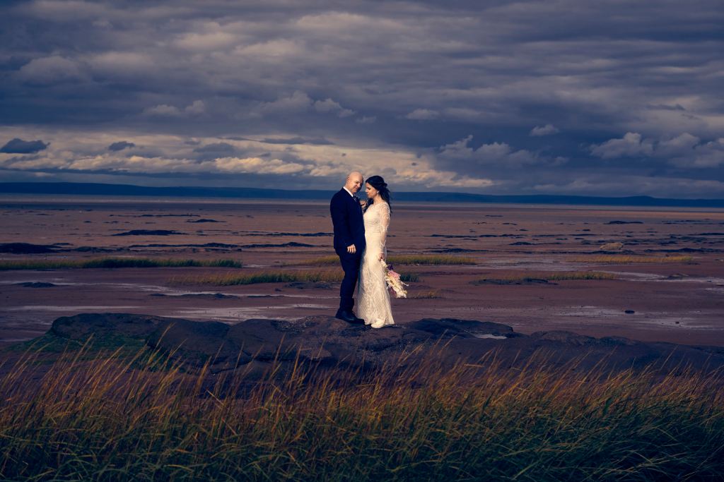 Bride and groom standing together in a dramatic coastal landscape